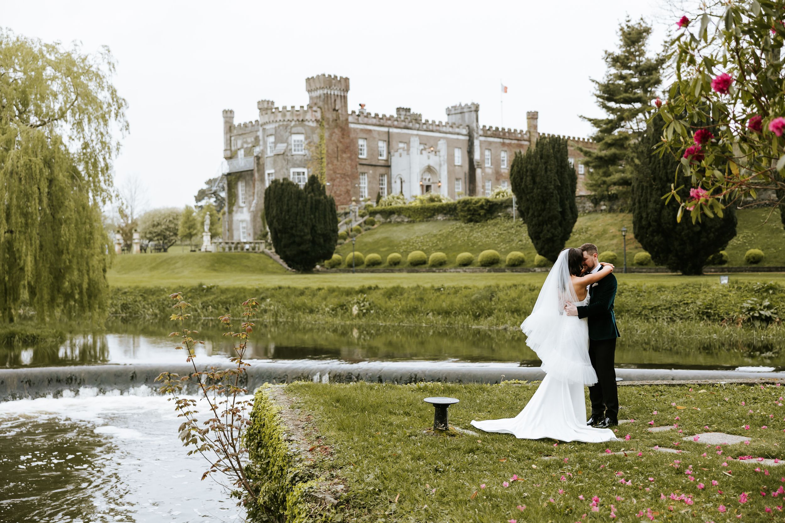 Romantic wedding couple poses in elegant garden setting with castle and lake. Bellingham Castle Conlon Photo & Film
