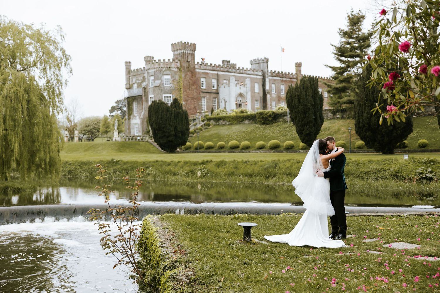 Romantic wedding couple poses in elegant garden setting with castle and lake. Bellingham Castle Conlon Photo & Film