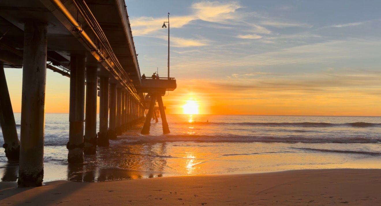 Dramatic sunset silhouettes the San Clemente Pier while golden light reflects off the ocean waves in California.