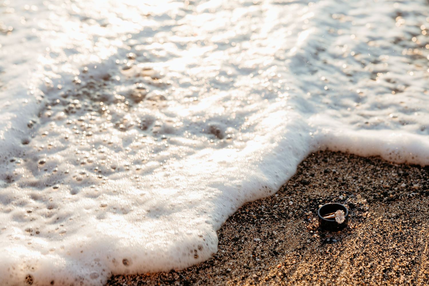 Gentle ocean waves washing up on sandy beach with white foam creating a natural pattern along the shoreline.