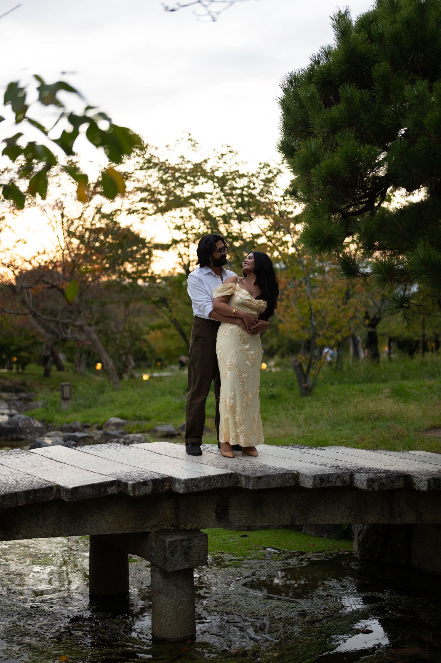 Couple embraces on a stone bridge at sunset in a Japanese garden.