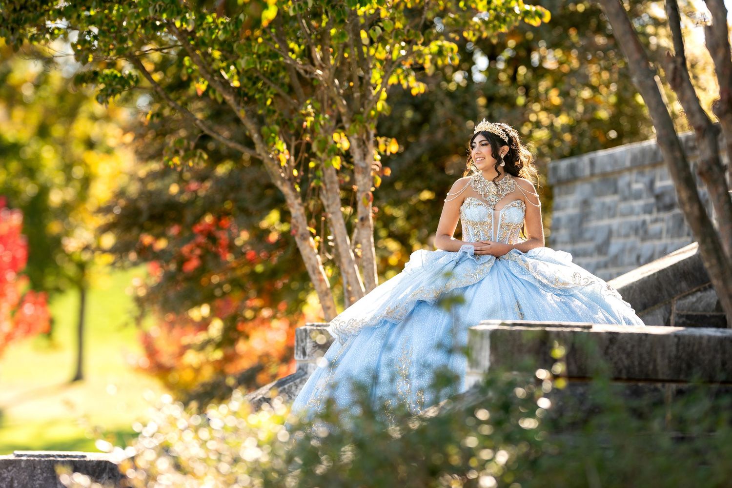 Young woman in elegant light blue quinceanera ball gown in garden.
