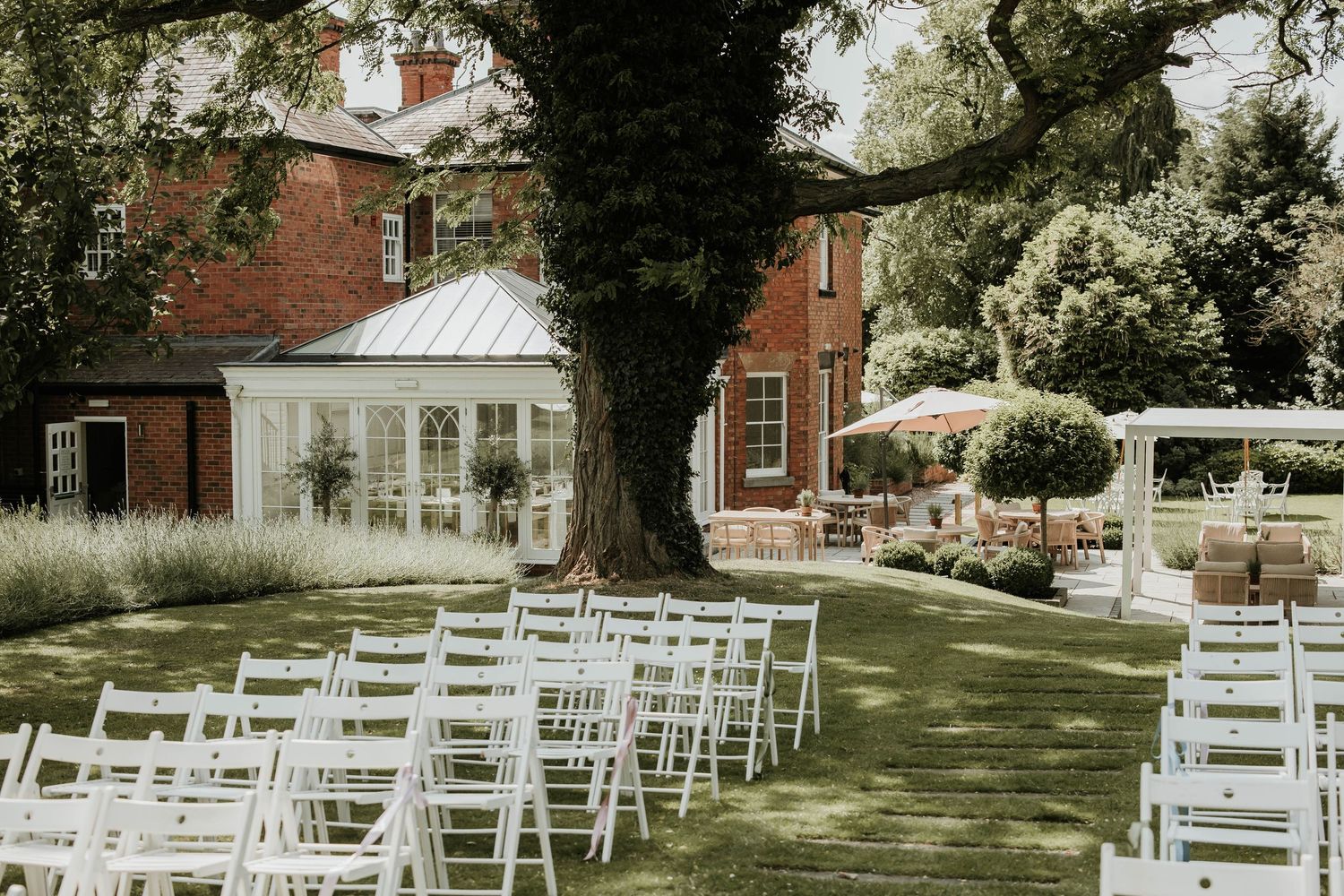White wooden chairs arranged in rows on a lush green lawn for an outdoor garden wedding ceremony. Vicarage boutique, Southwell