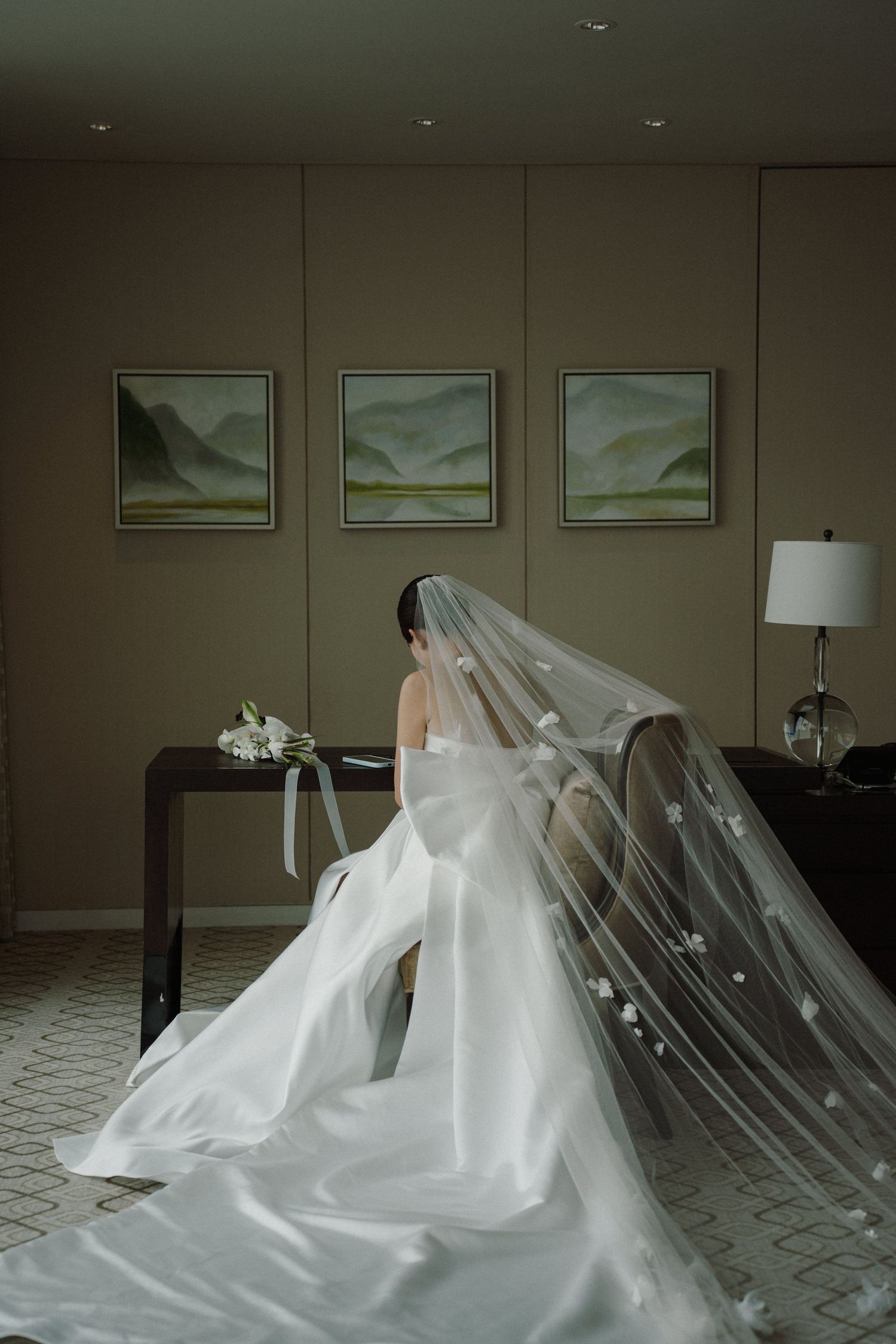 A flowing white wedding dress and veil photographed in a hotel room with artwork.