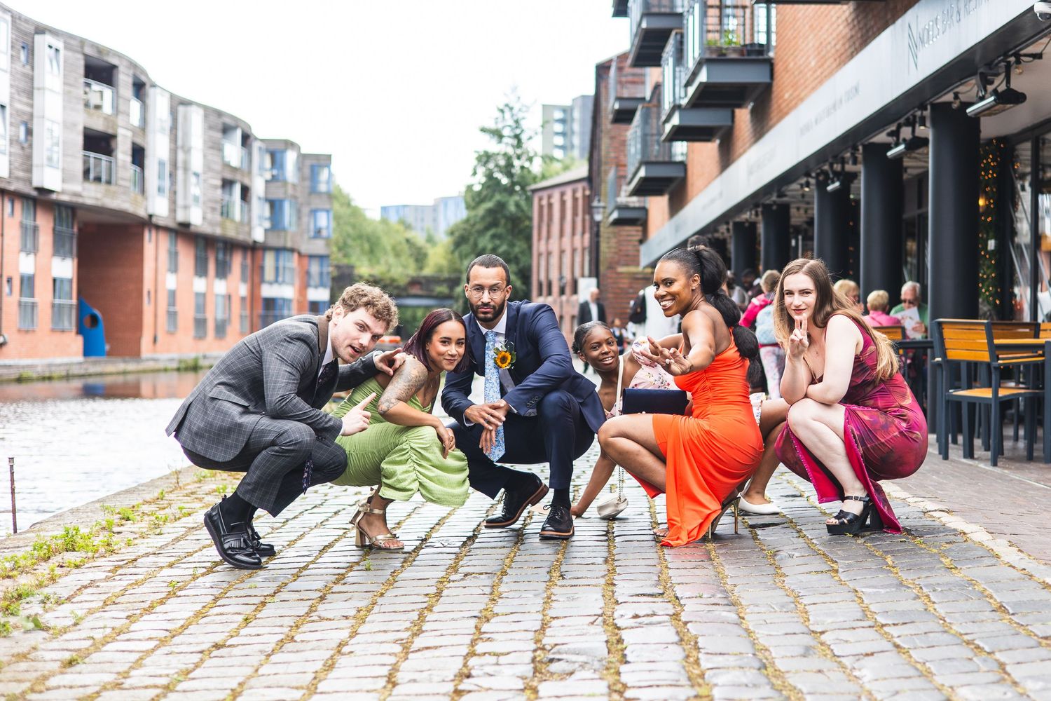 Group of dancers practicing street dance moves in an urban setting with brick buildings in the background.