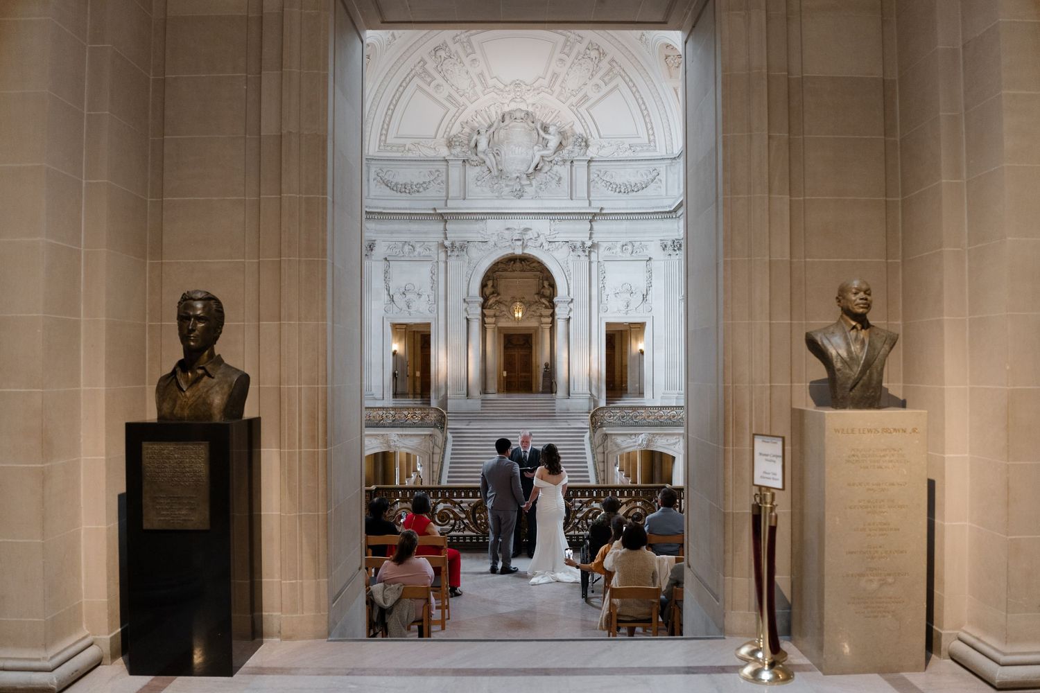 An elegant museum hallway with marble columns, arched ceilings, and sculptures on pedestals lining the walls.