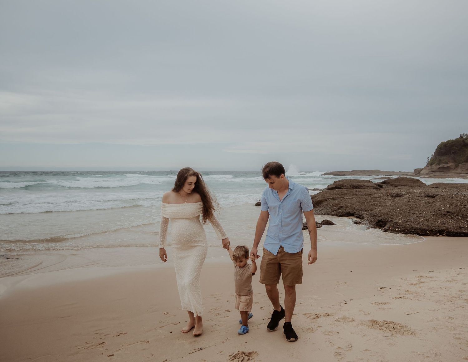 Couple walking along a misty beach shoreline during overcast weather.