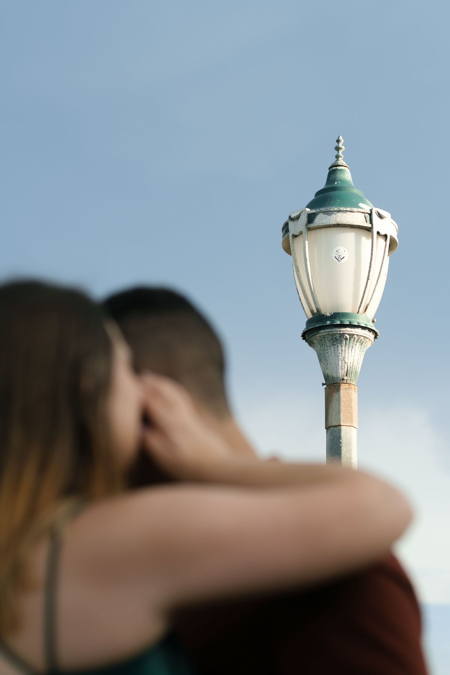 Vintage-style ornate street lamp post with green and white details against a soft blue sky.