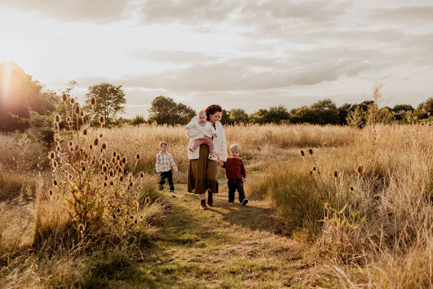 A family wrapped in plaid blankets poses together in a golden autumn field on an overcast day.