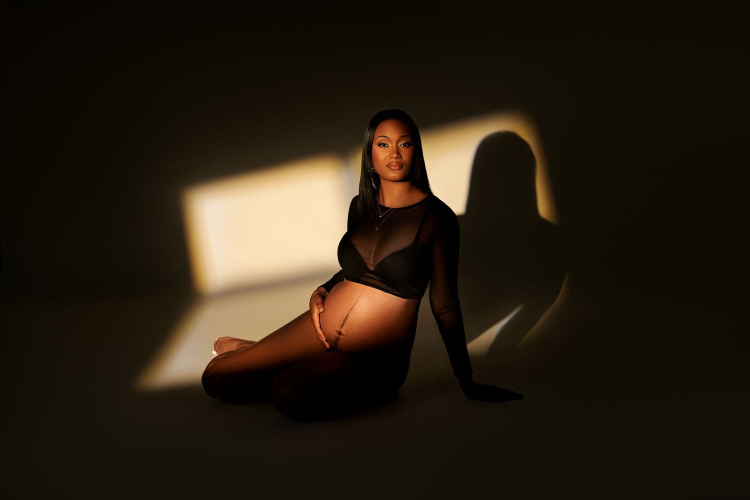 A dramatic maternity photo with moody lighting and strong shadows against a dark background.