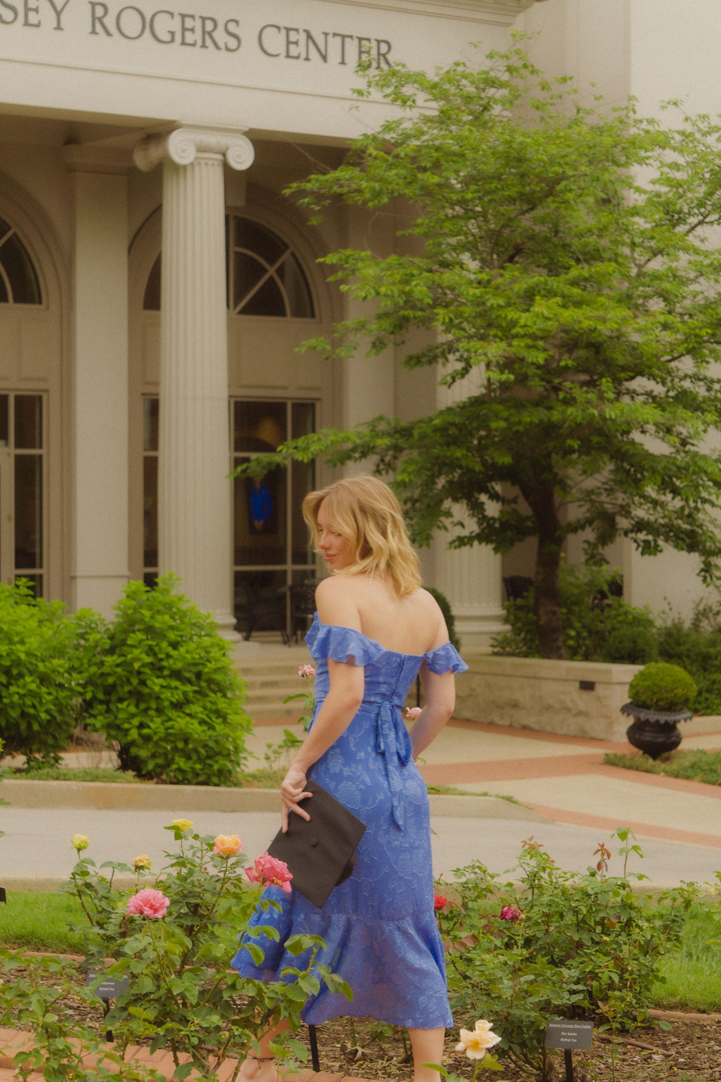 Blue dress graduation photos taken in front of the Rogers Center building with flowering bushes.