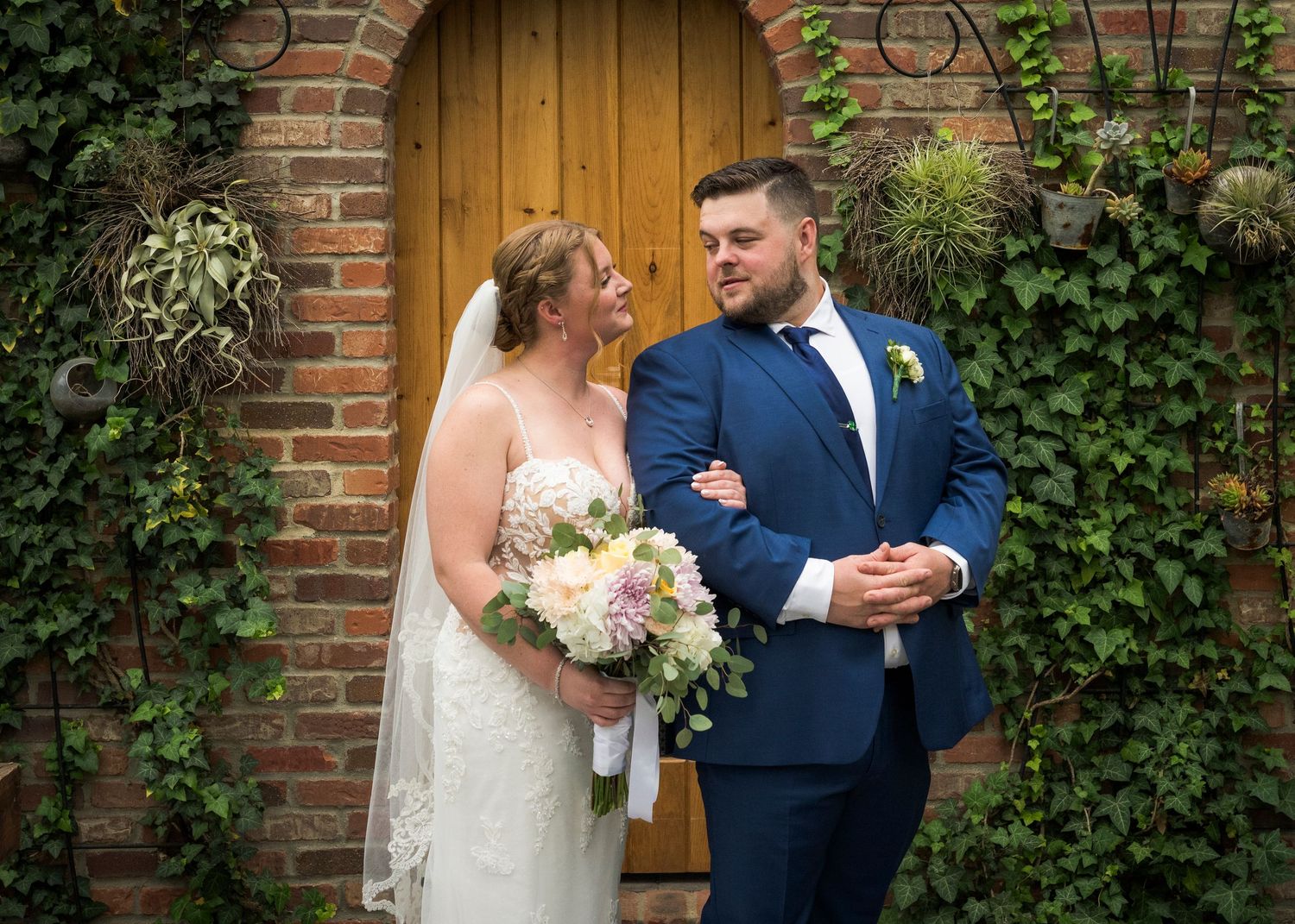 Newlyweds share an intimate moment outdoors with autumn foliage and rustic architecture in background.