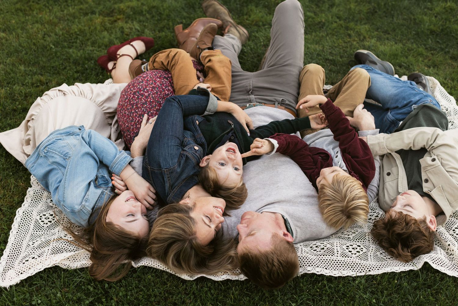 A happy family wearing fall colors tickles each other while laying on a cream crochet blanket for family photos in Stratham, Seacoast NH.
