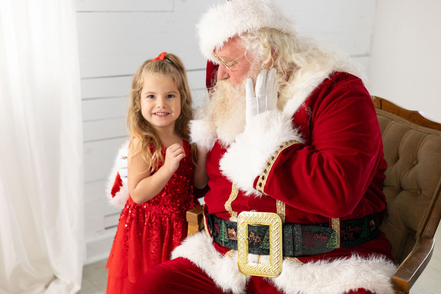 A young child in a red dress visits with Santa Claus in a festive holiday portrait setting. Lifestyle Family Photography Tacoma WA