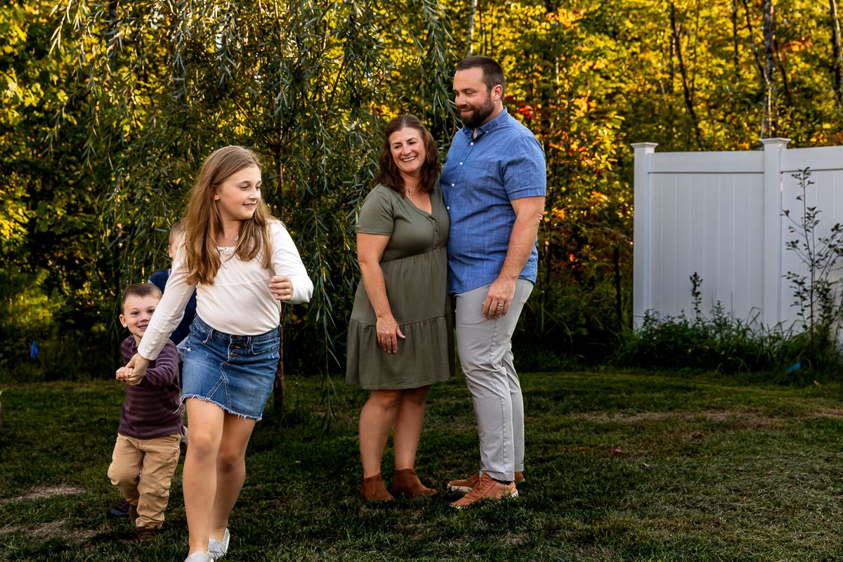 A family enjoying outdoor time together in a backyard with autumn trees and golden sunlight in the background.