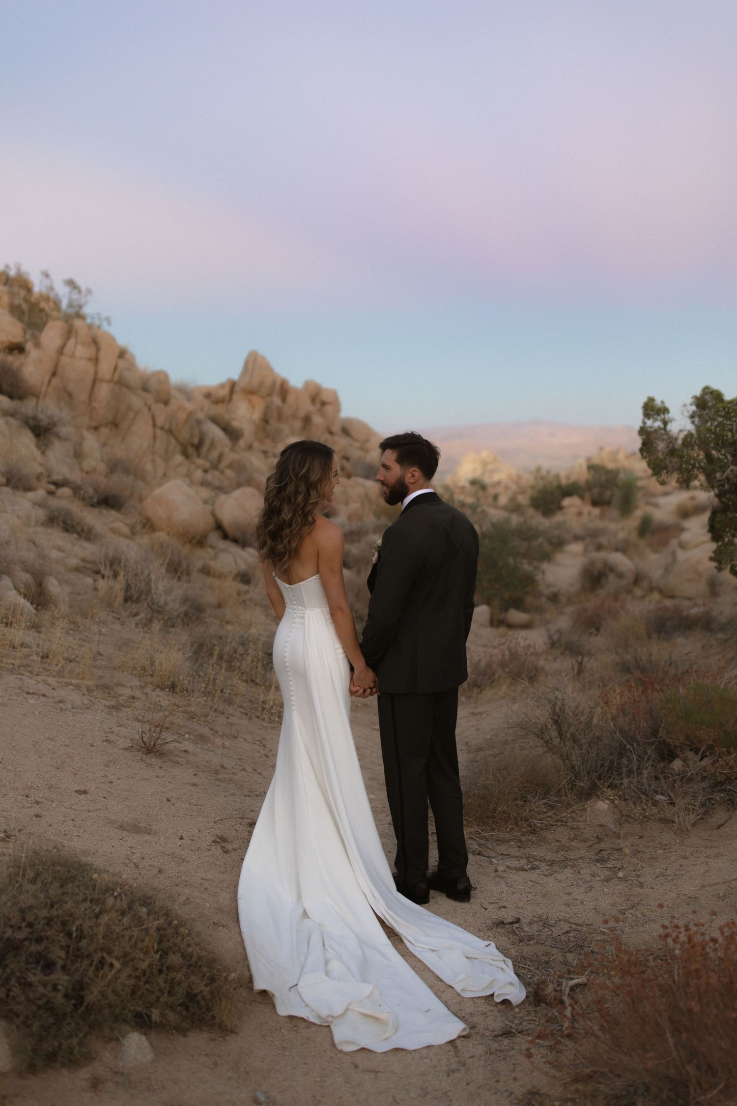 Wedding couple shares intimate moments amidst desert landscape with large rock formations at sunset.