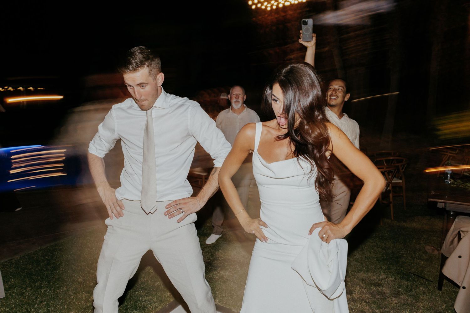 Wedding guests dance on an outdoor dance floor during a nighttime reception celebration.
