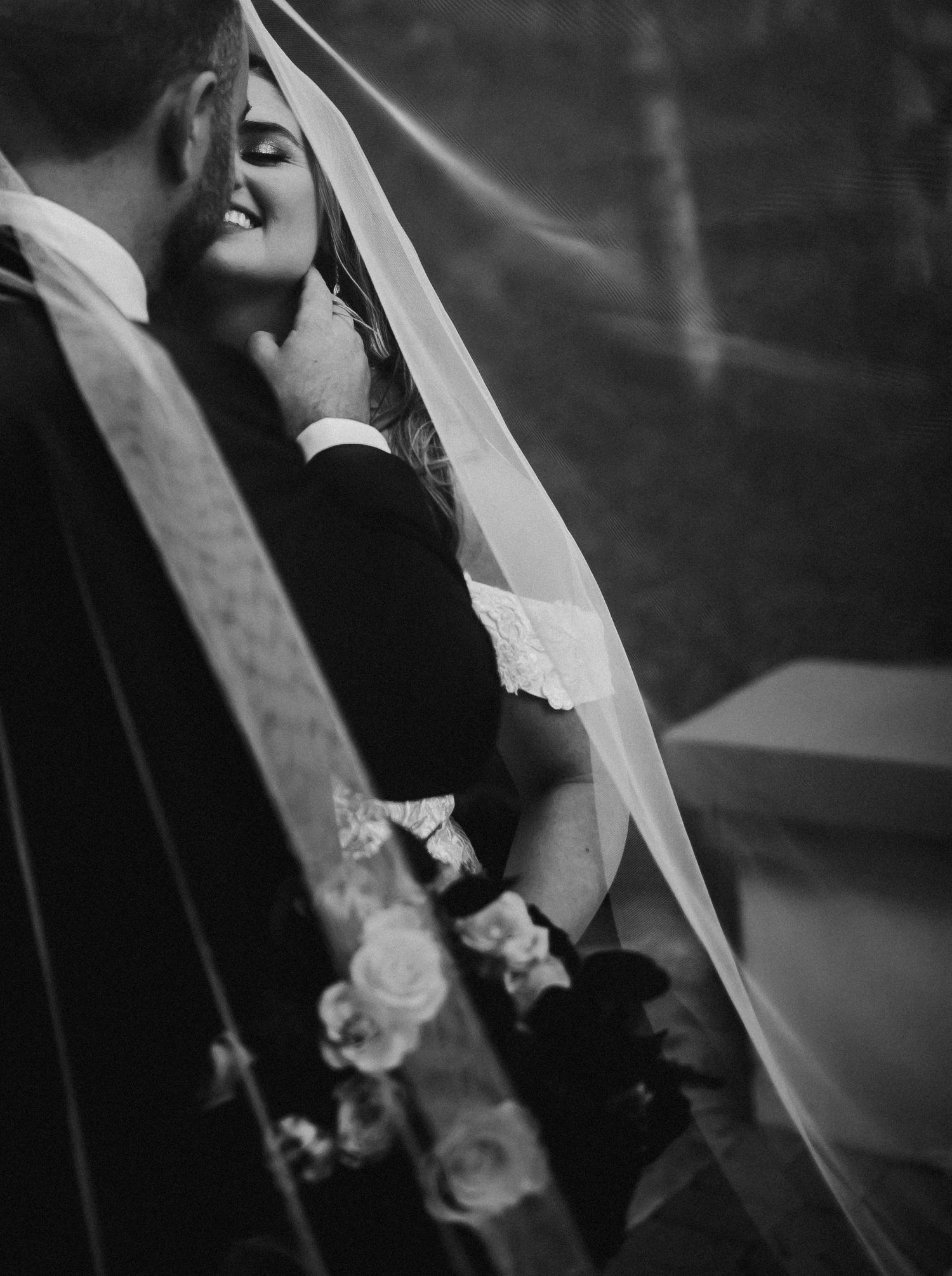 Black and white image showing delicate lace details of a bride's veil and wedding attire.