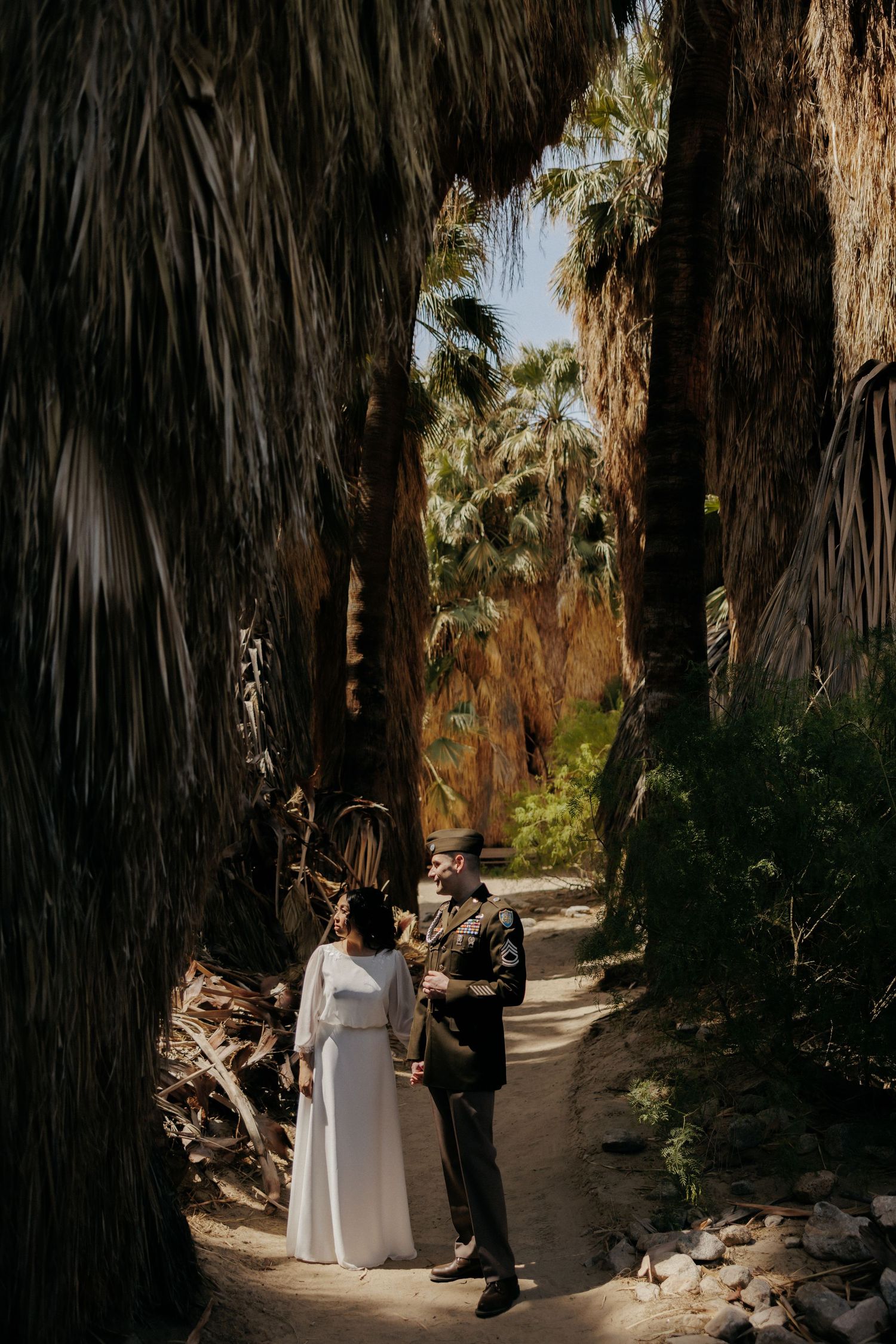 A pathway through tall palm trees and desert vegetation during a wedding ceremony at an oasis.