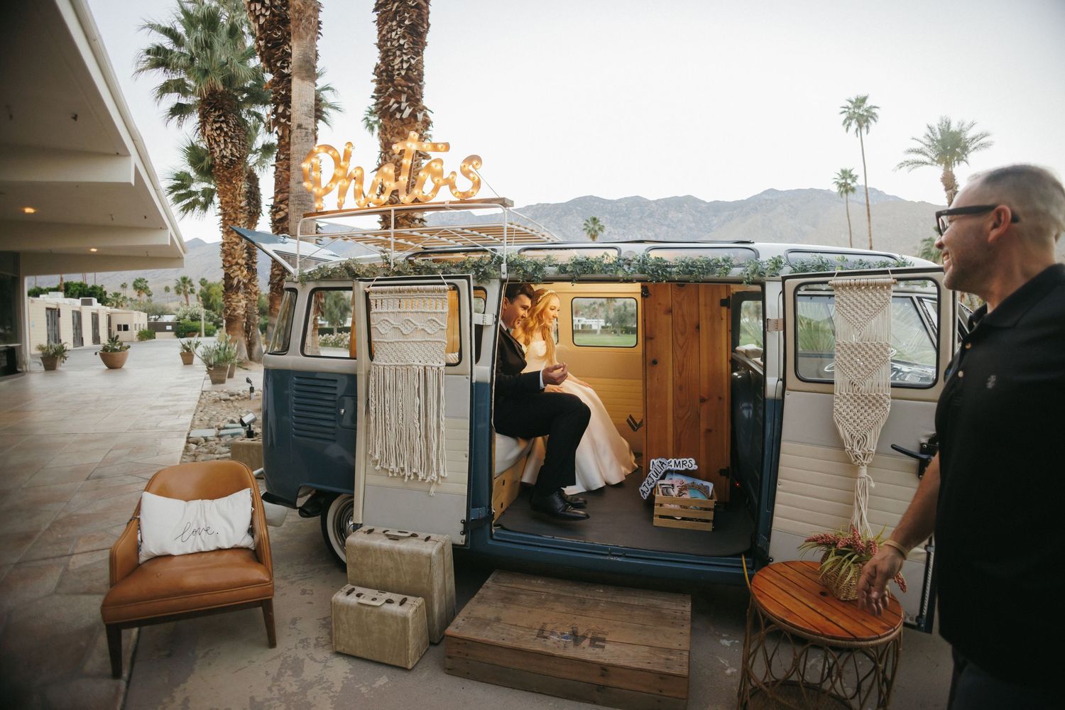 Bride and groom sitting inside a vintage VW bus photo booth decorated with macrame at sunset.