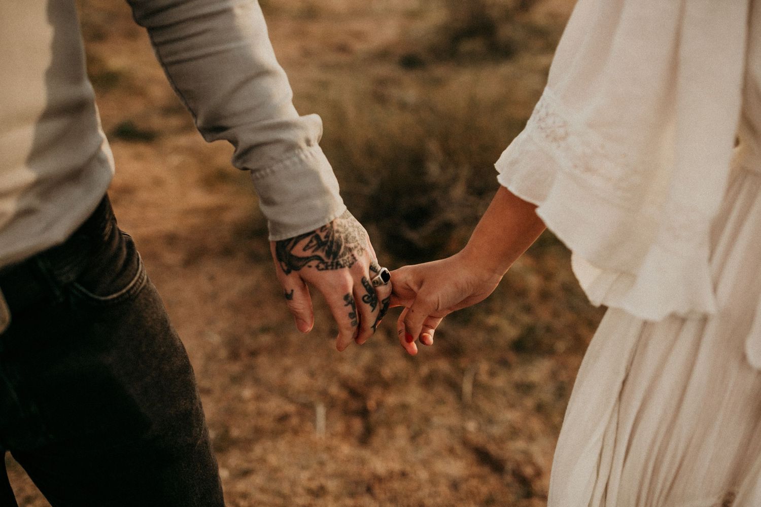 A couple's hands intertwined in a warm embrace, displaying their wedding rings against an earthy brown background.