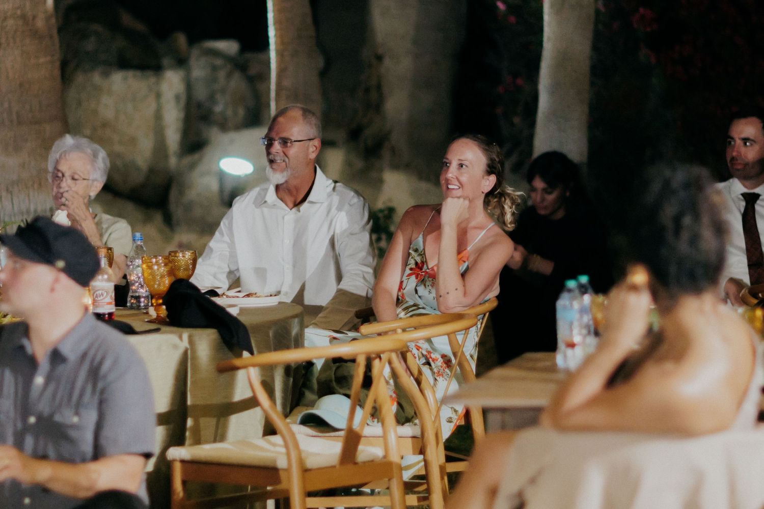 Wedding guests enjoying a casual outdoor reception at rustic venue with wooden tables and warm lighting.