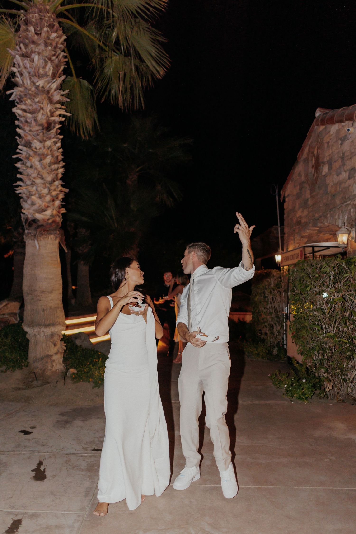 Couple dancing together outdoors at night among palm trees during a celebration.