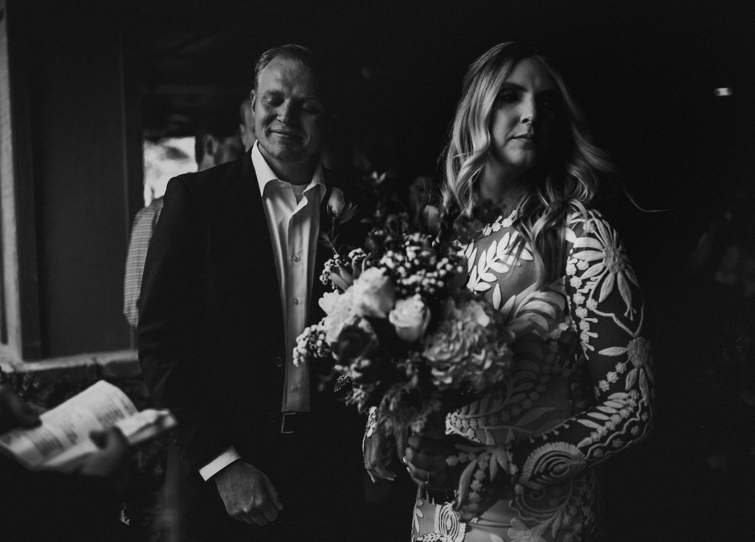 A black and white wedding photo showing two people walking together, with one holding a beautiful bouquet of flowers.