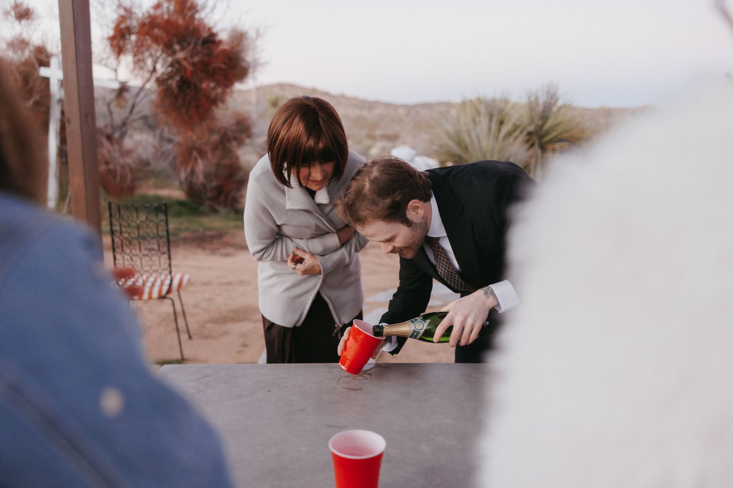 Wedding guests leaning over a table playing a game with red Solo cups at an outdoor desert reception.