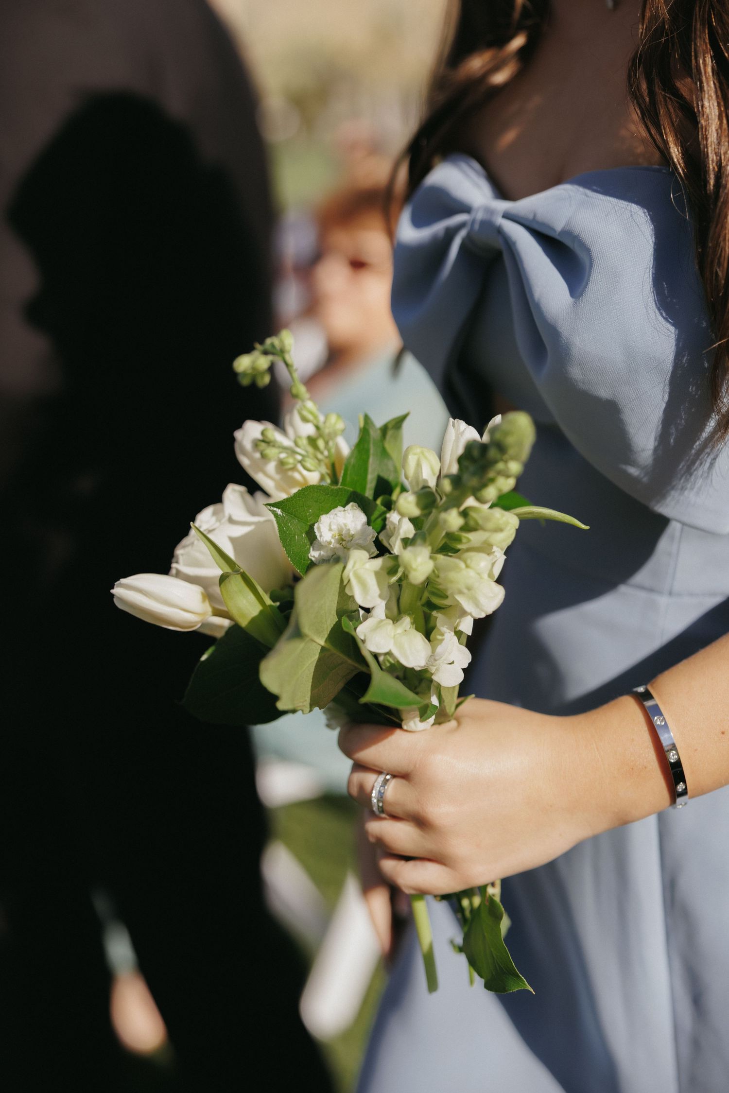 Bridesmaid in blue dress holding white tulip and flower bouquet at wedding ceremony.