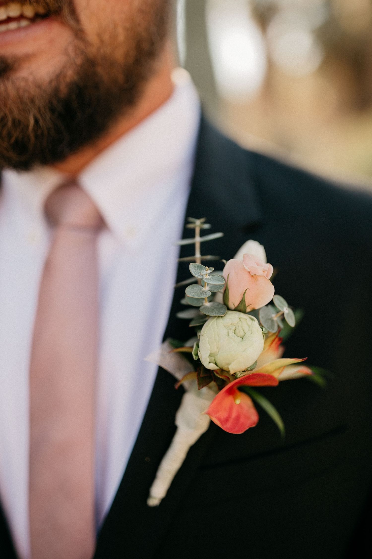 Row of matching pink rose boutonnieres pinned to dark suit lapels at formal wedding event.