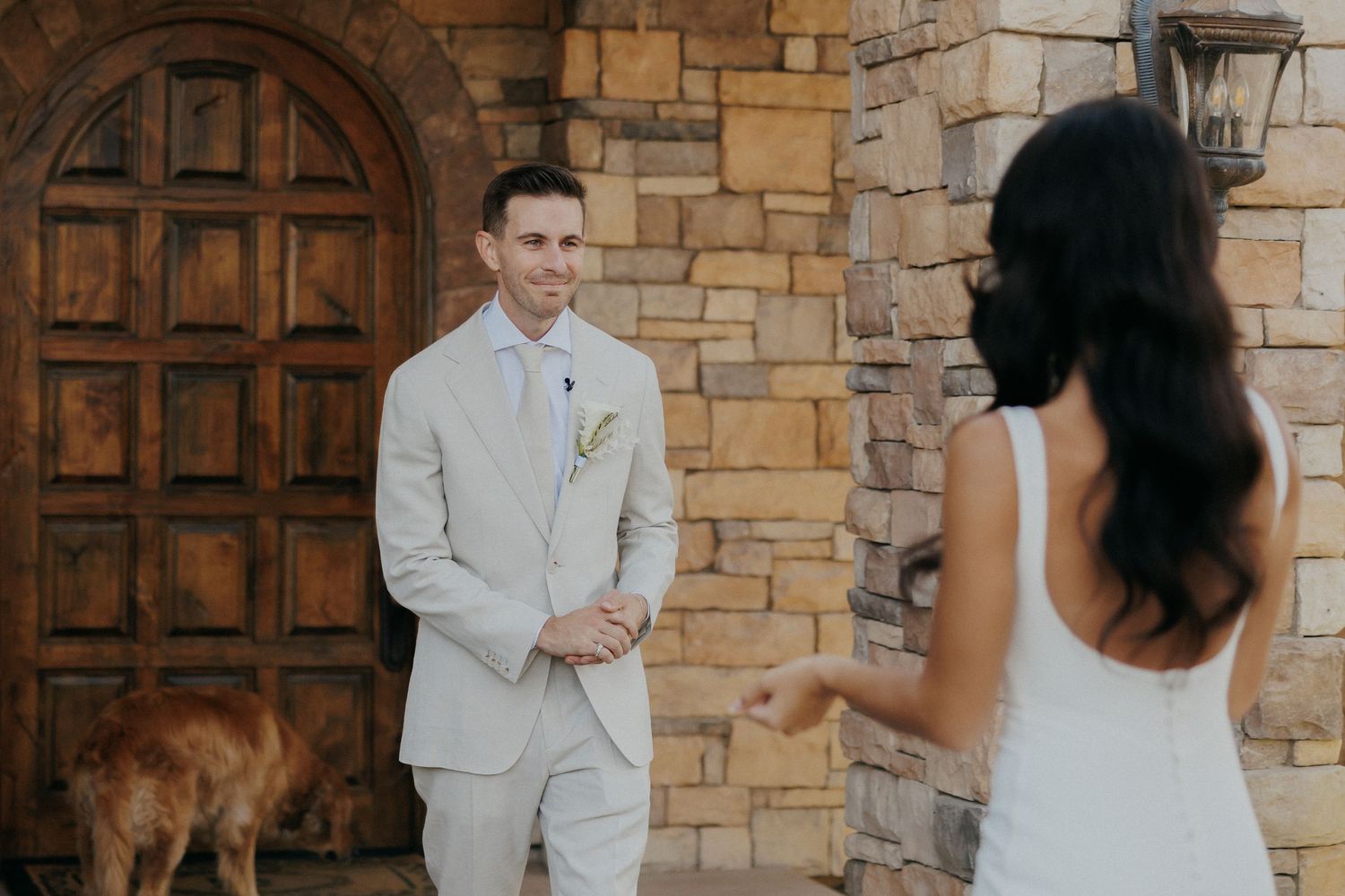 Romantic wedding couple stands beside rustic stone wall during outdoor ceremony.
