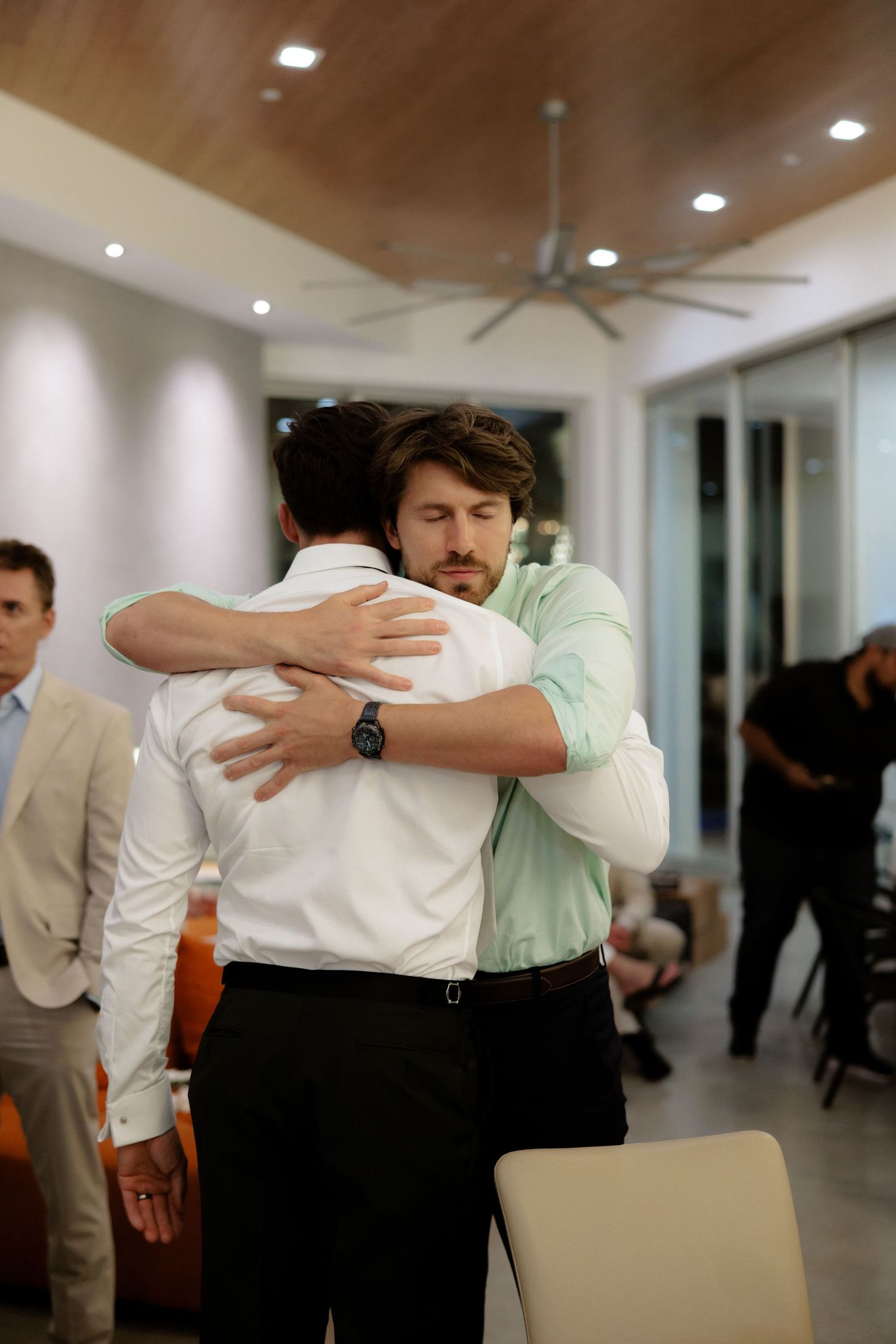 Business colleagues greet each other with professional back pats in a modern office hallway.