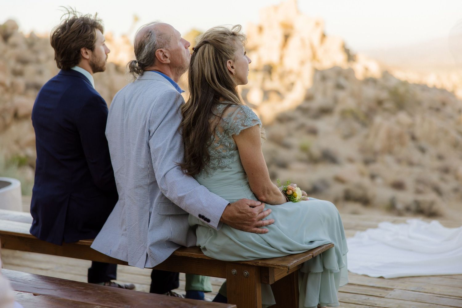 Romantic couple embraces on wooden bench at sunset in desert landscape with mountains in background.