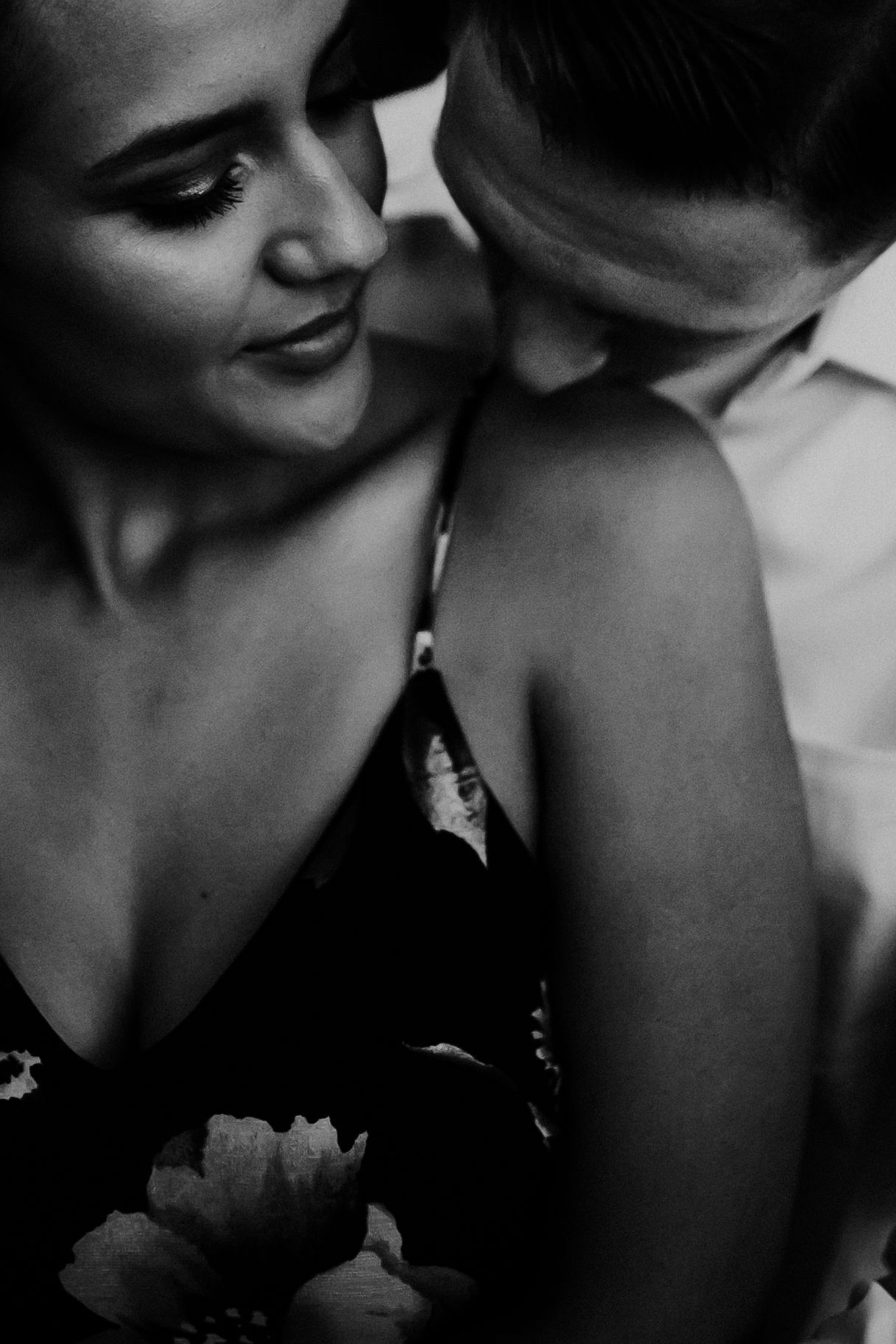 A romantic black and white close-up portrait showing an intimate moment between a couple in moody lighting.