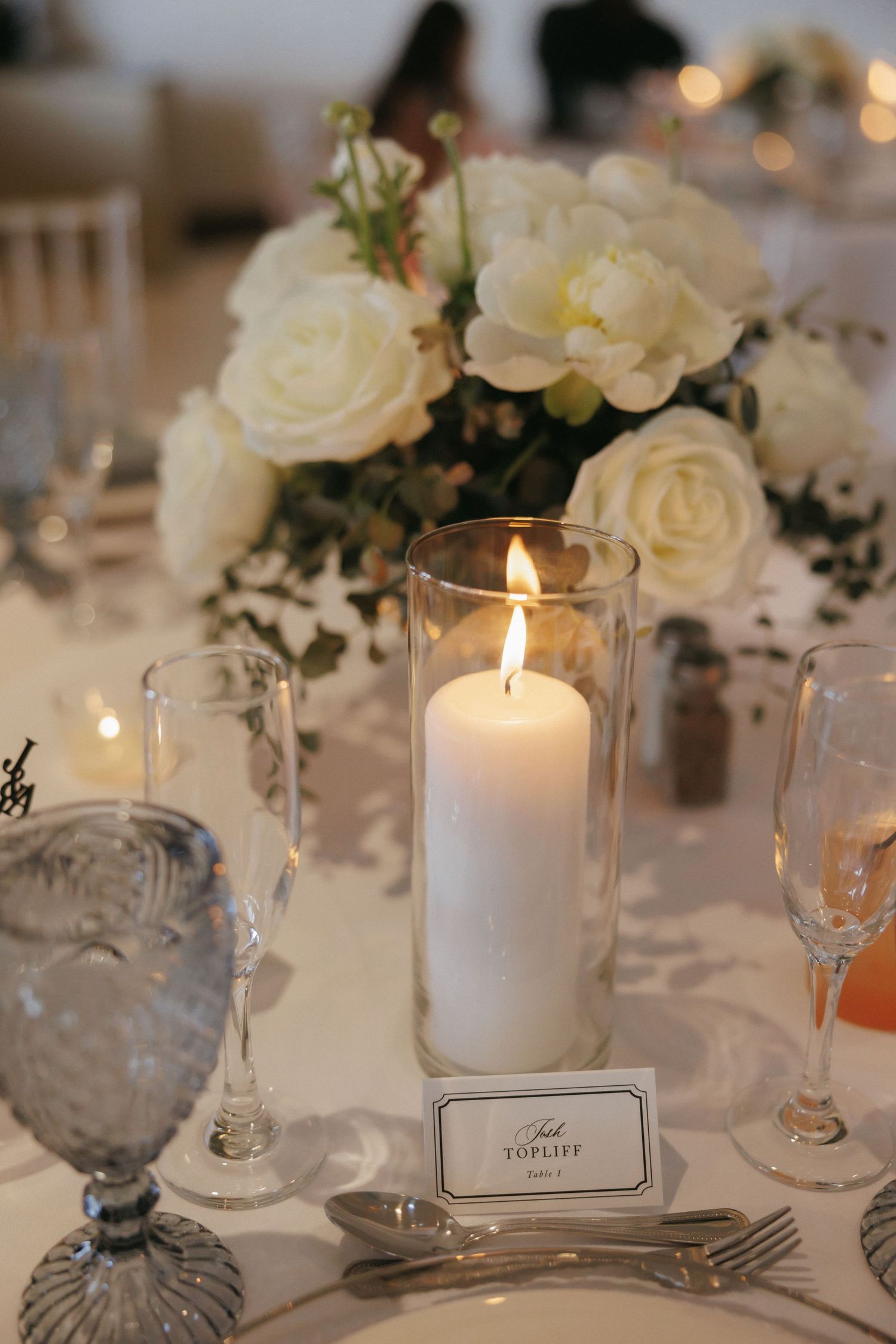 Elegant wedding reception table with white pillar candle, roses, and crystal glassware.
