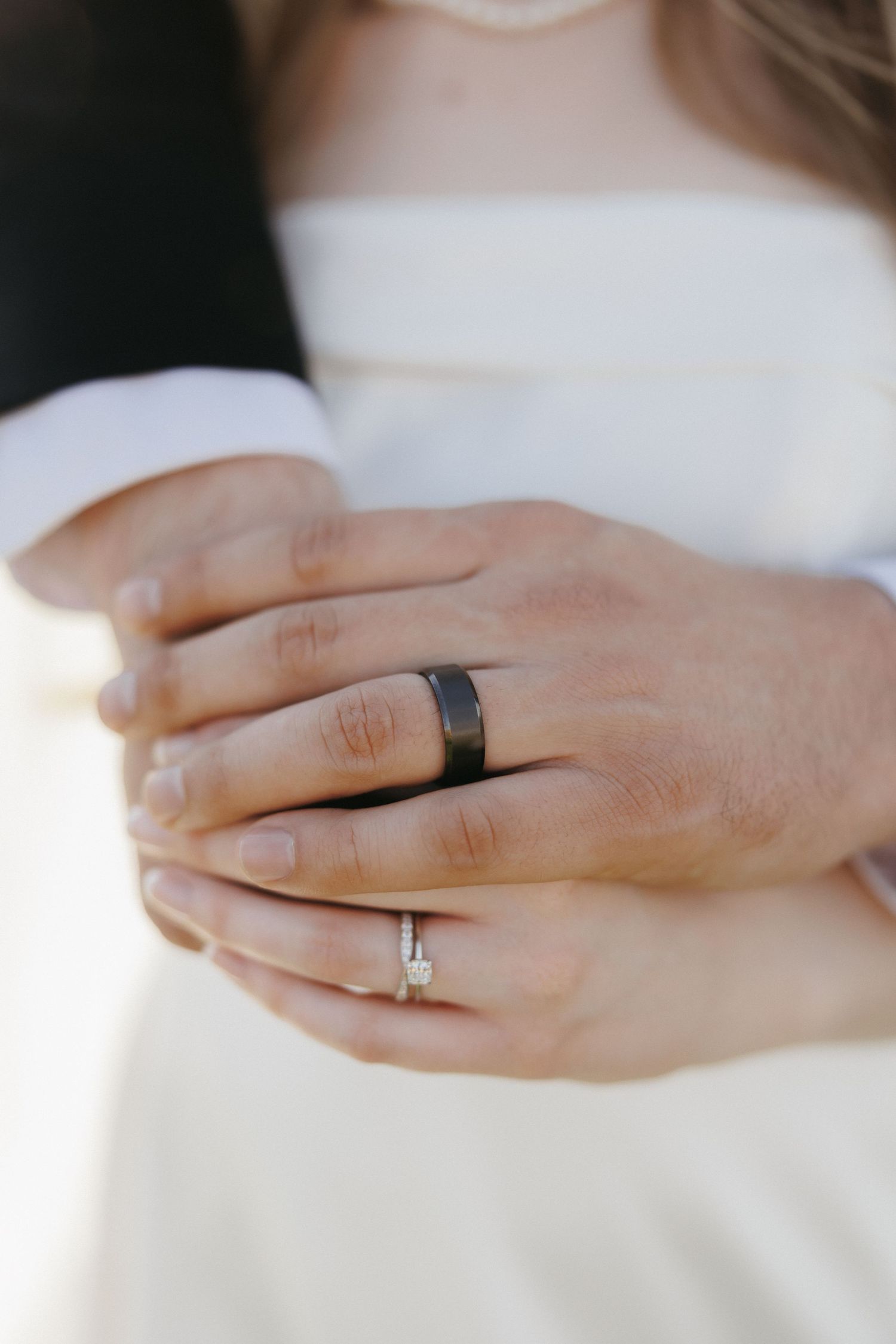 Close-up of bride and groom hands showing wedding rings, black band and diamond engagement ring.