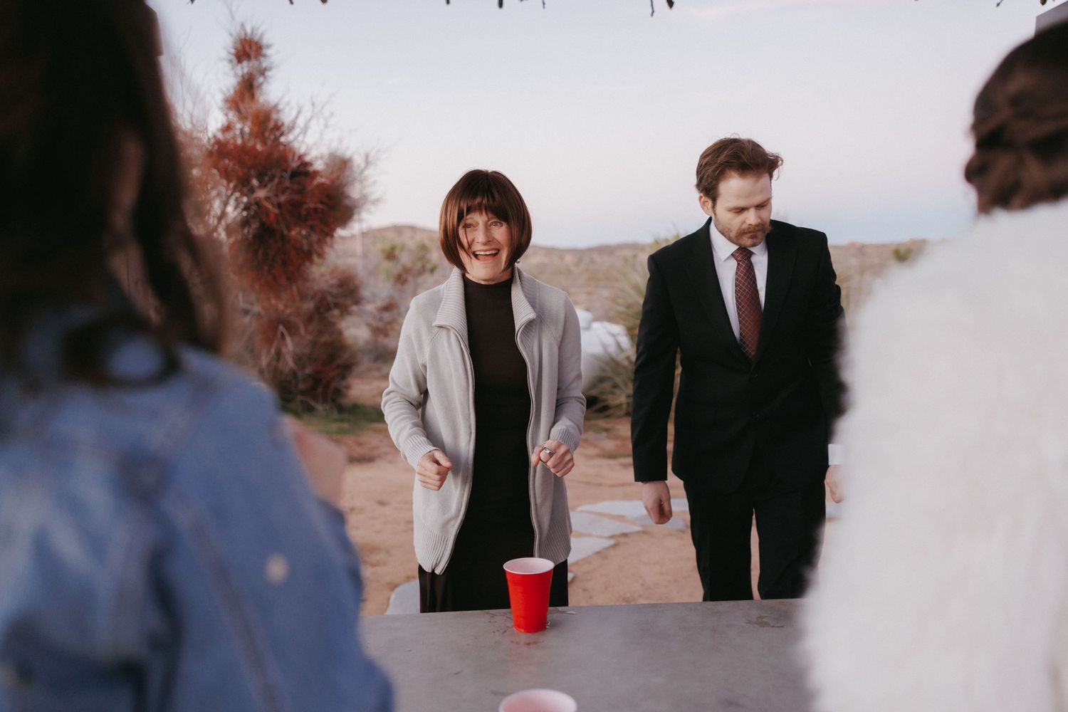 Wedding guests play beer pong at outdoor desert reception at dusk.
