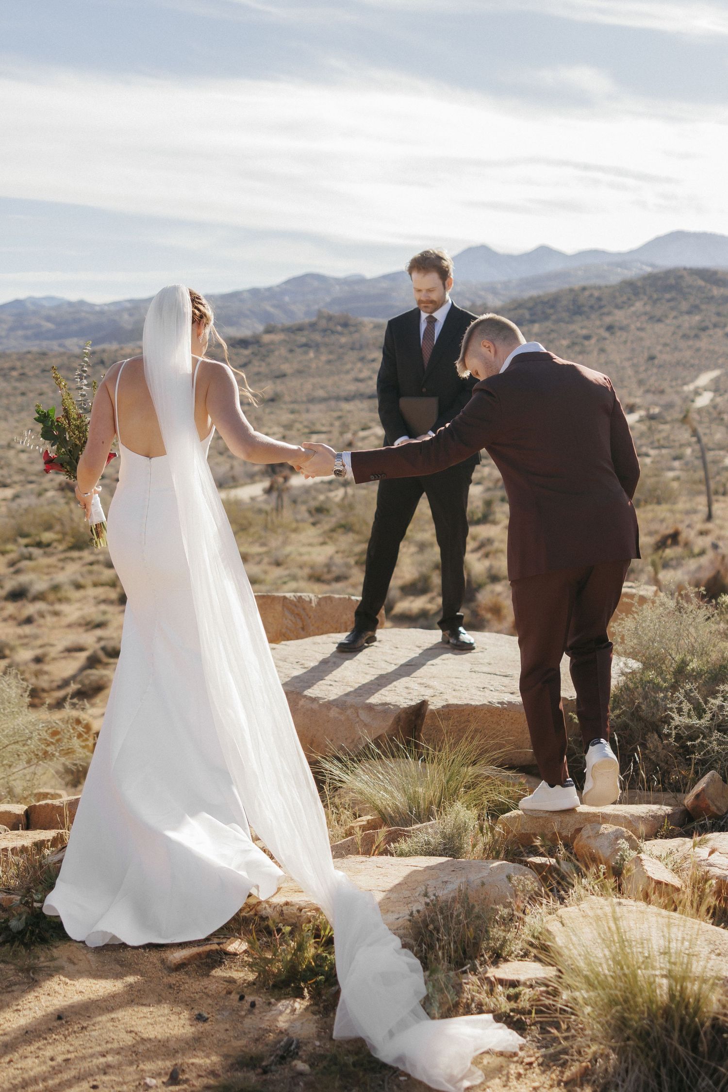 Bride and groom exchange vows outdoors in desert landscape with officiant during rustic elopement ceremony.