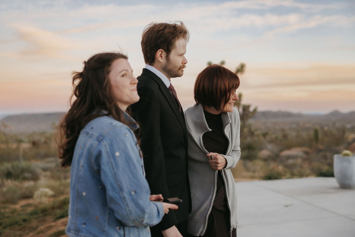 Three wedding guests gaze at a colorful desert sunset over the Joshua Tree landscape from a rooftop.