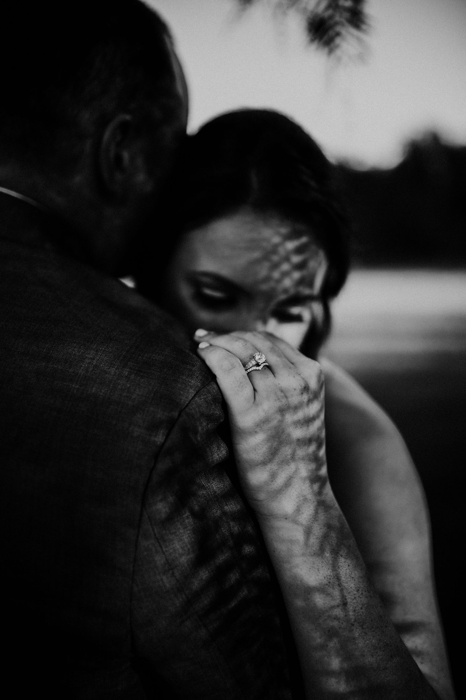 Artistic black and white photograph showing shadows of tree branches cast across an intimate couple embracing outdoors.