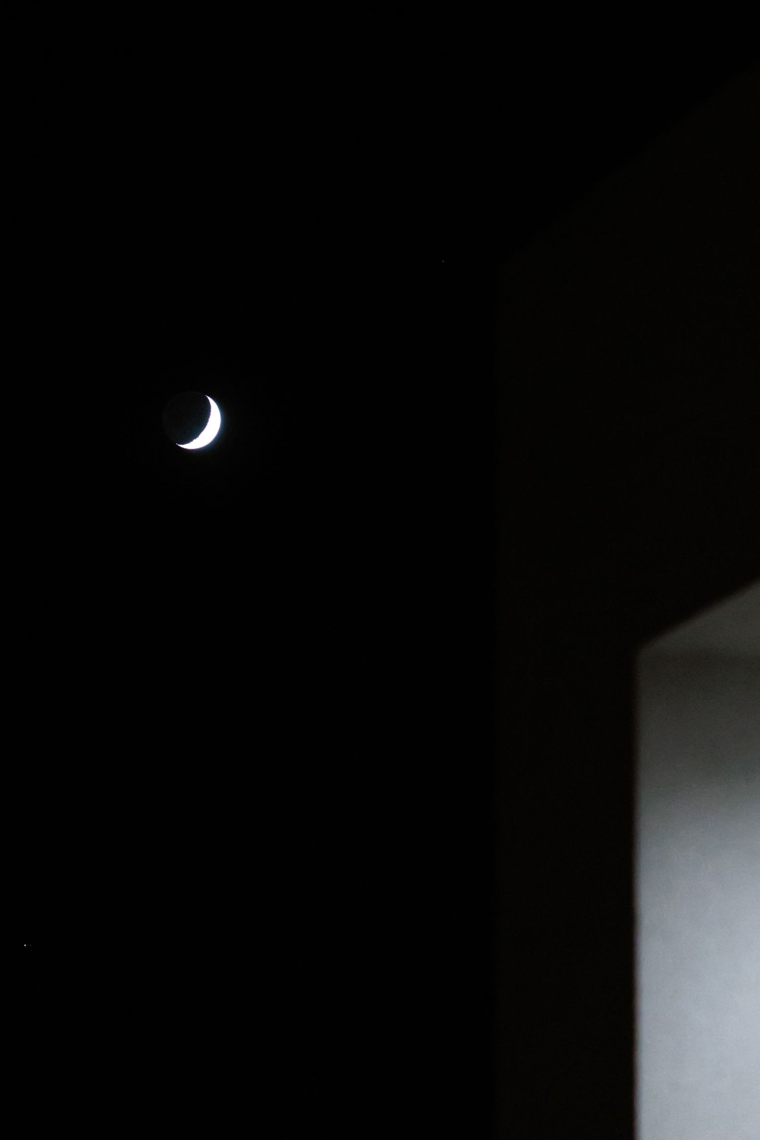 A crescent moon glows brightly against a dark night sky with architectural elements visible in silhouette.