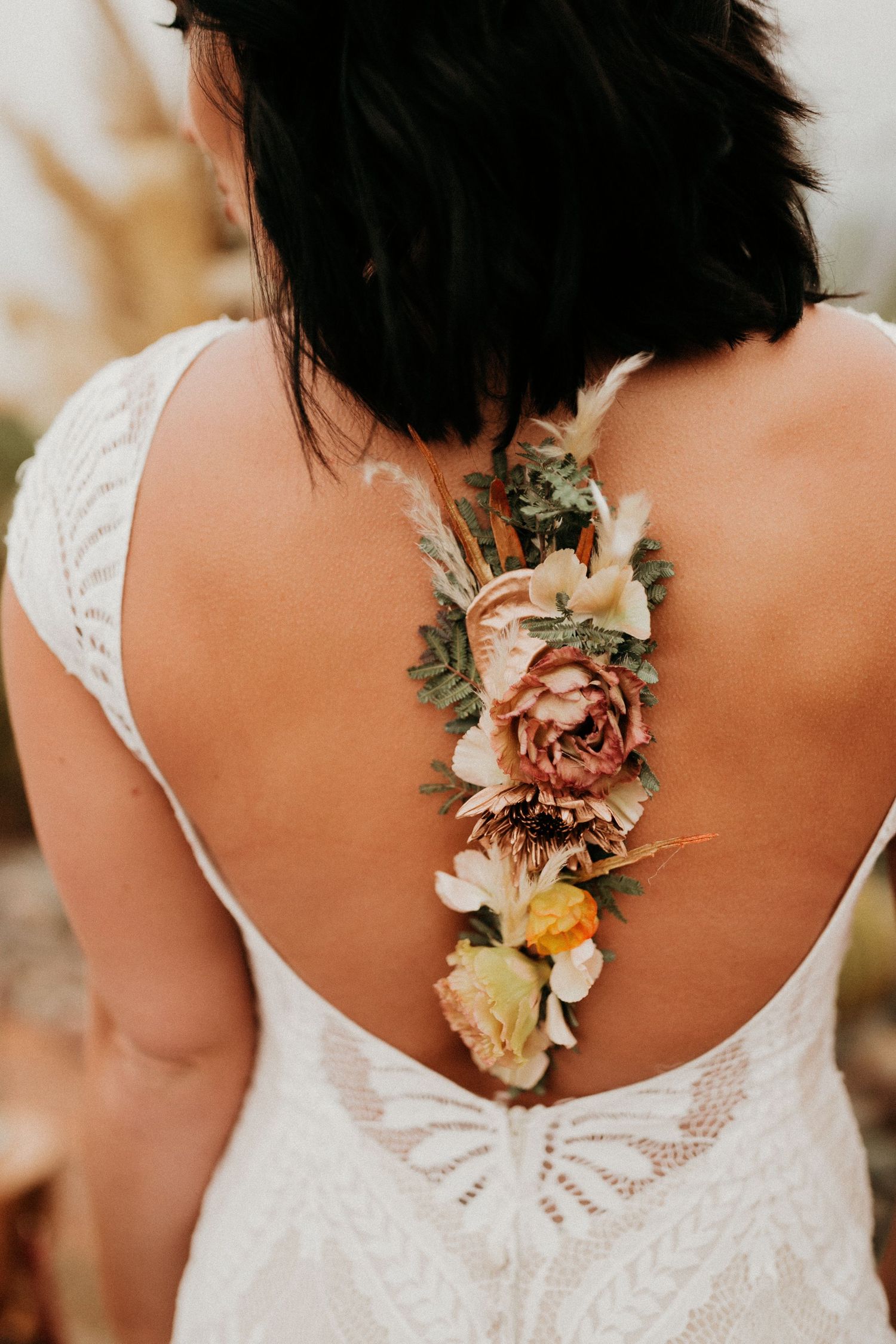 Close up of pink and orange floral details adorning the back of a white lace wedding dress.