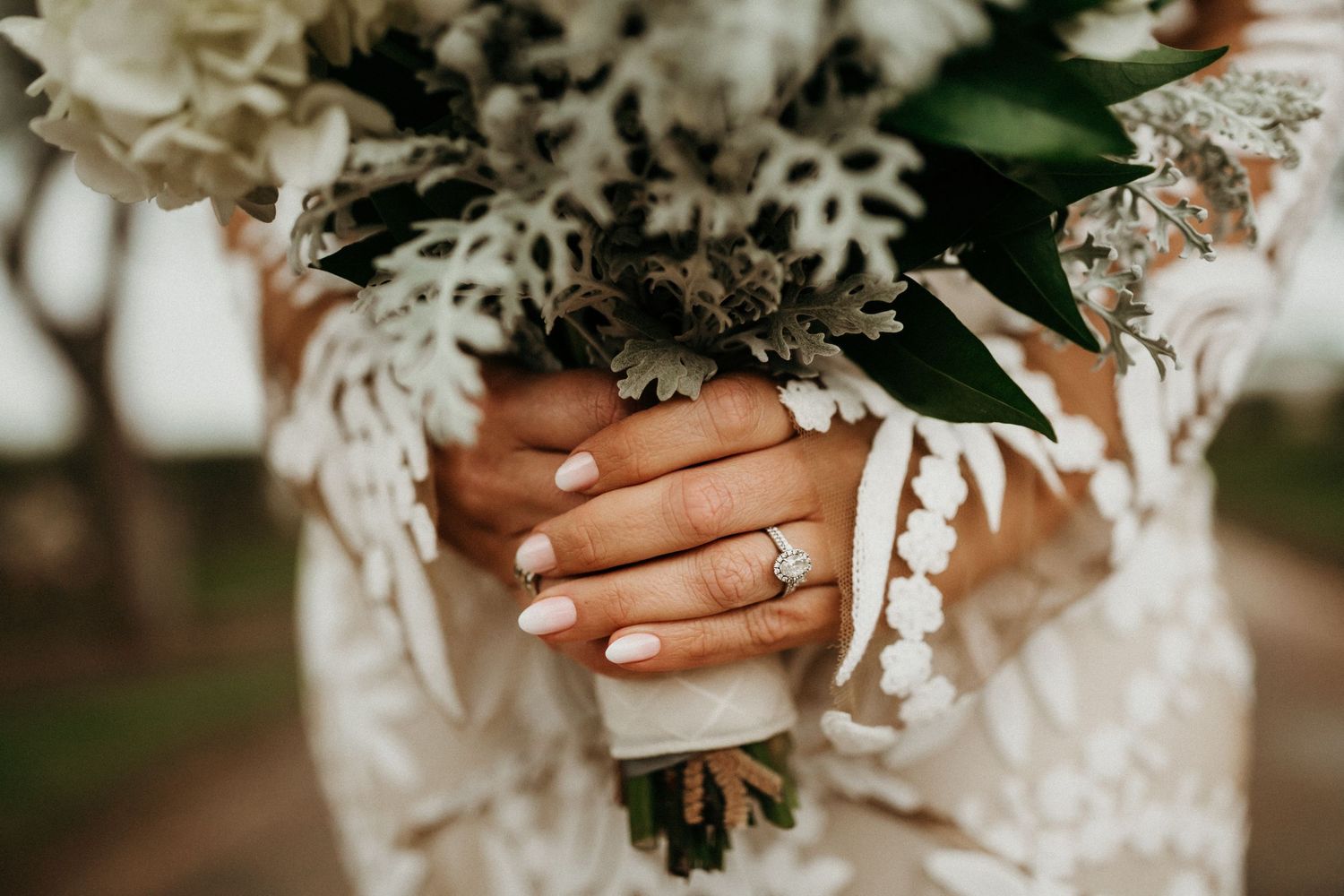 Wedding bouquet details showing white silk ribbon wrapped around floral stems against a romantic outdoor backdrop.