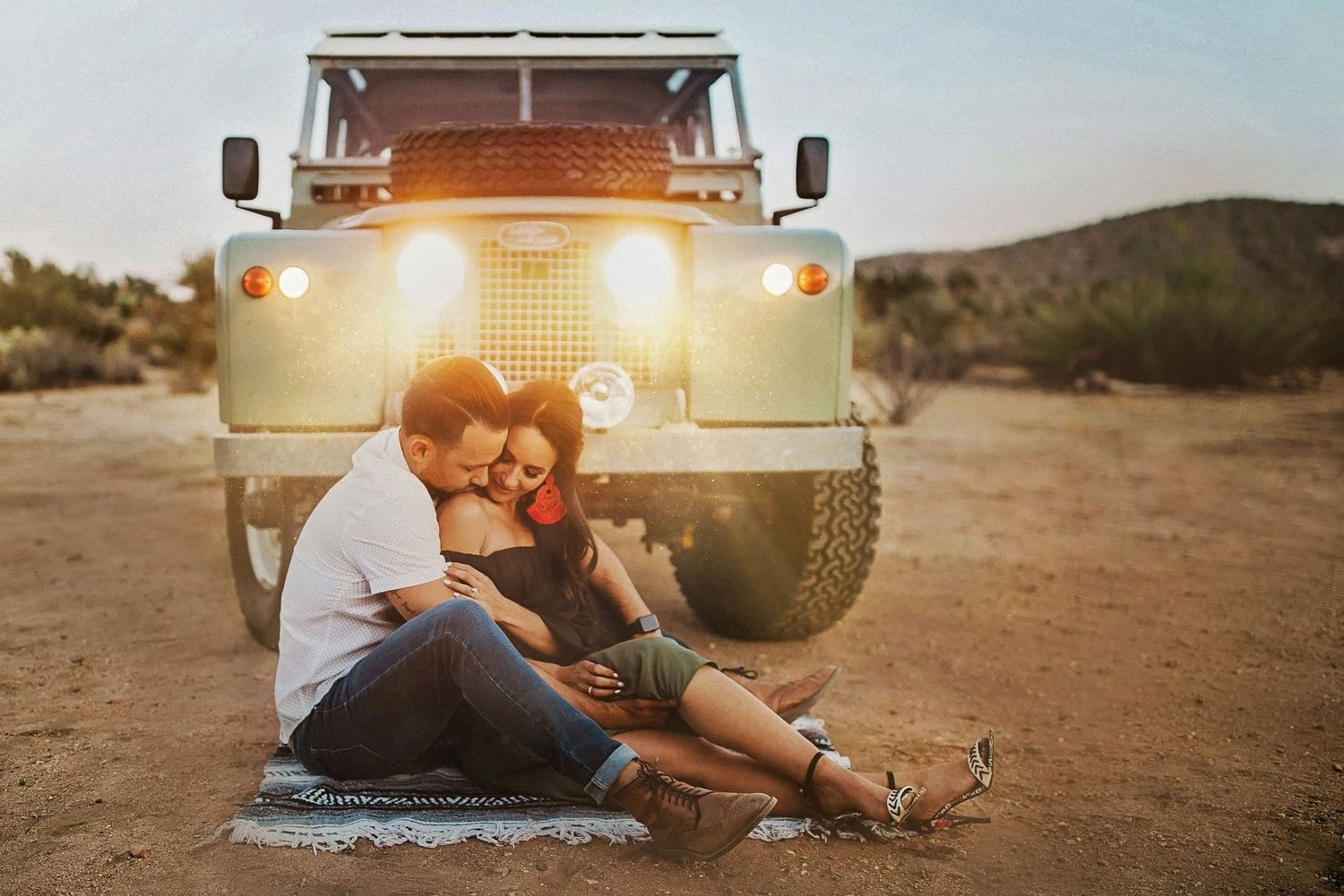A couple shares an intimate moment beside a vintage camper van at dusk in the desert.