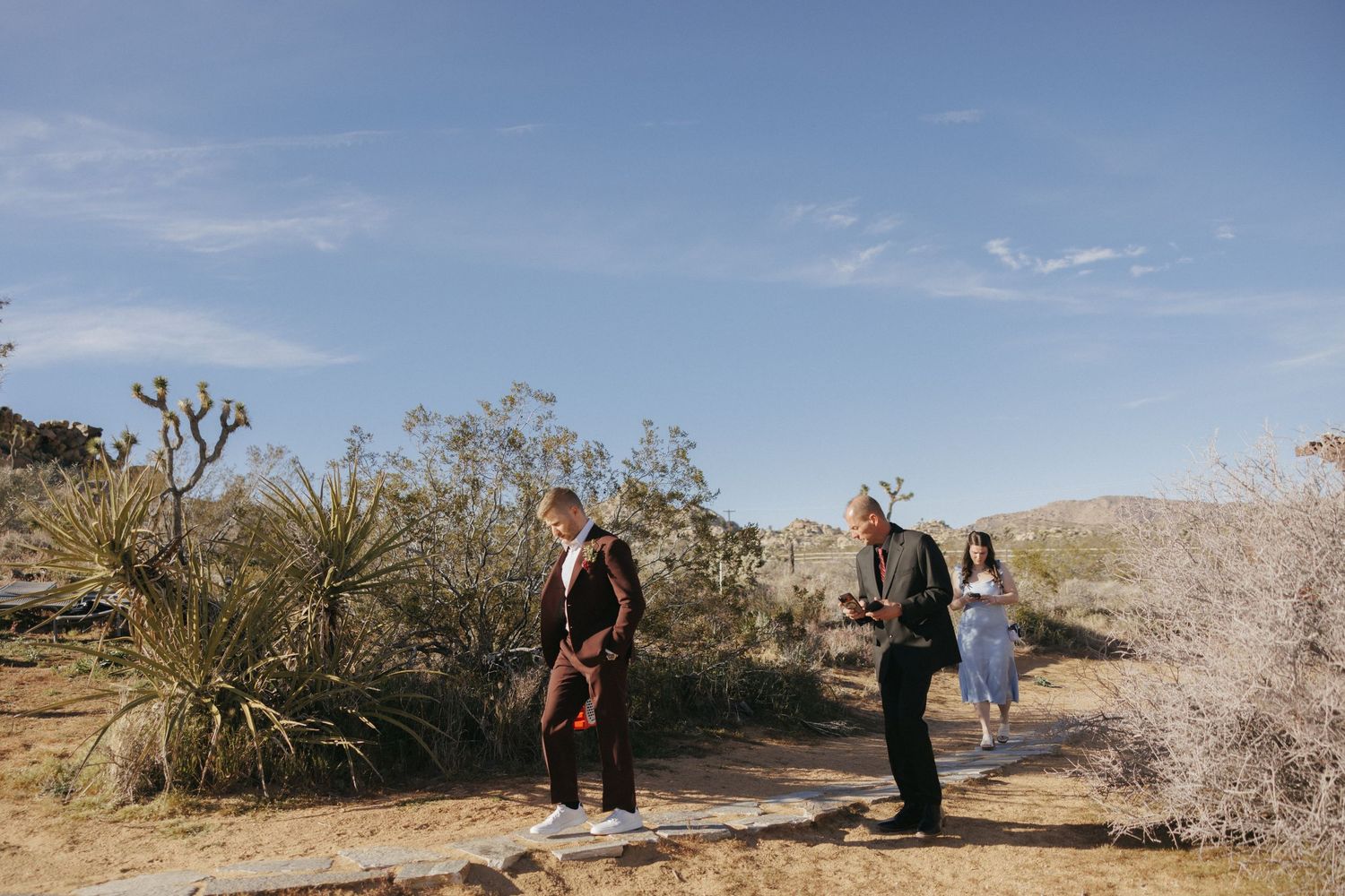Small wedding ceremony in Joshua Tree desert with officiant and guests among cacti under blue sky.