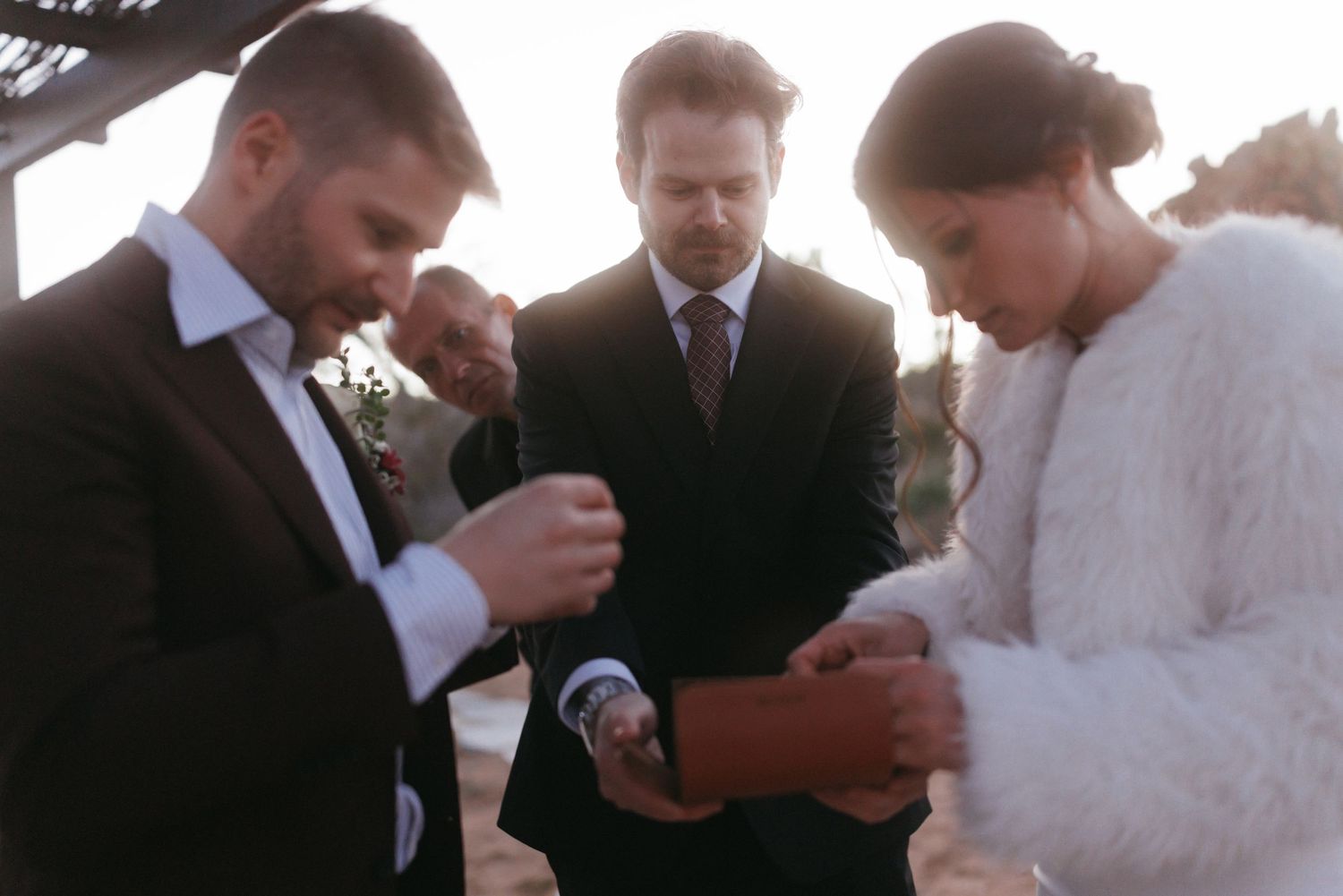 Couple exchanges rings during intimate outdoor wedding ceremony with officiant at sunset.