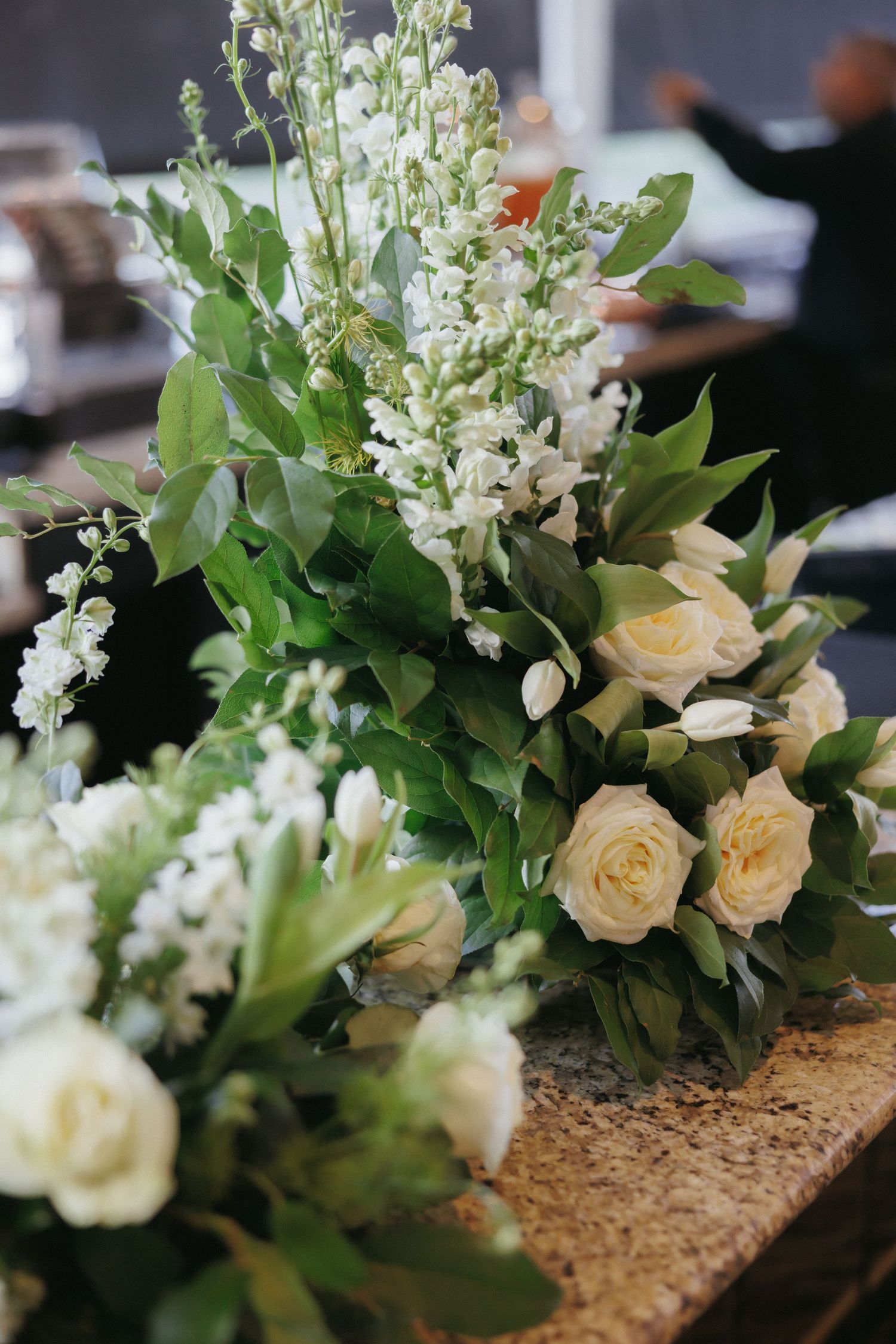 Elegant wedding floral arrangement of white roses and greenery displayed on granite surface indoors.