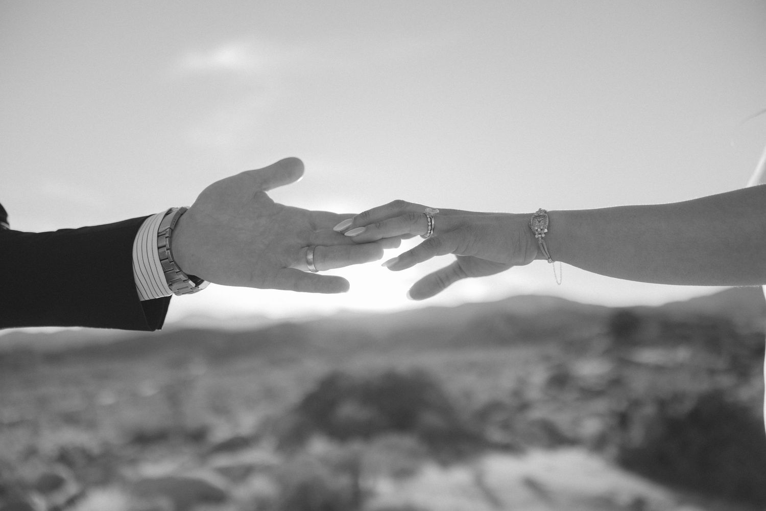 Black and white close-up of bride and groom reaching hands toward each other showing wedding ring.