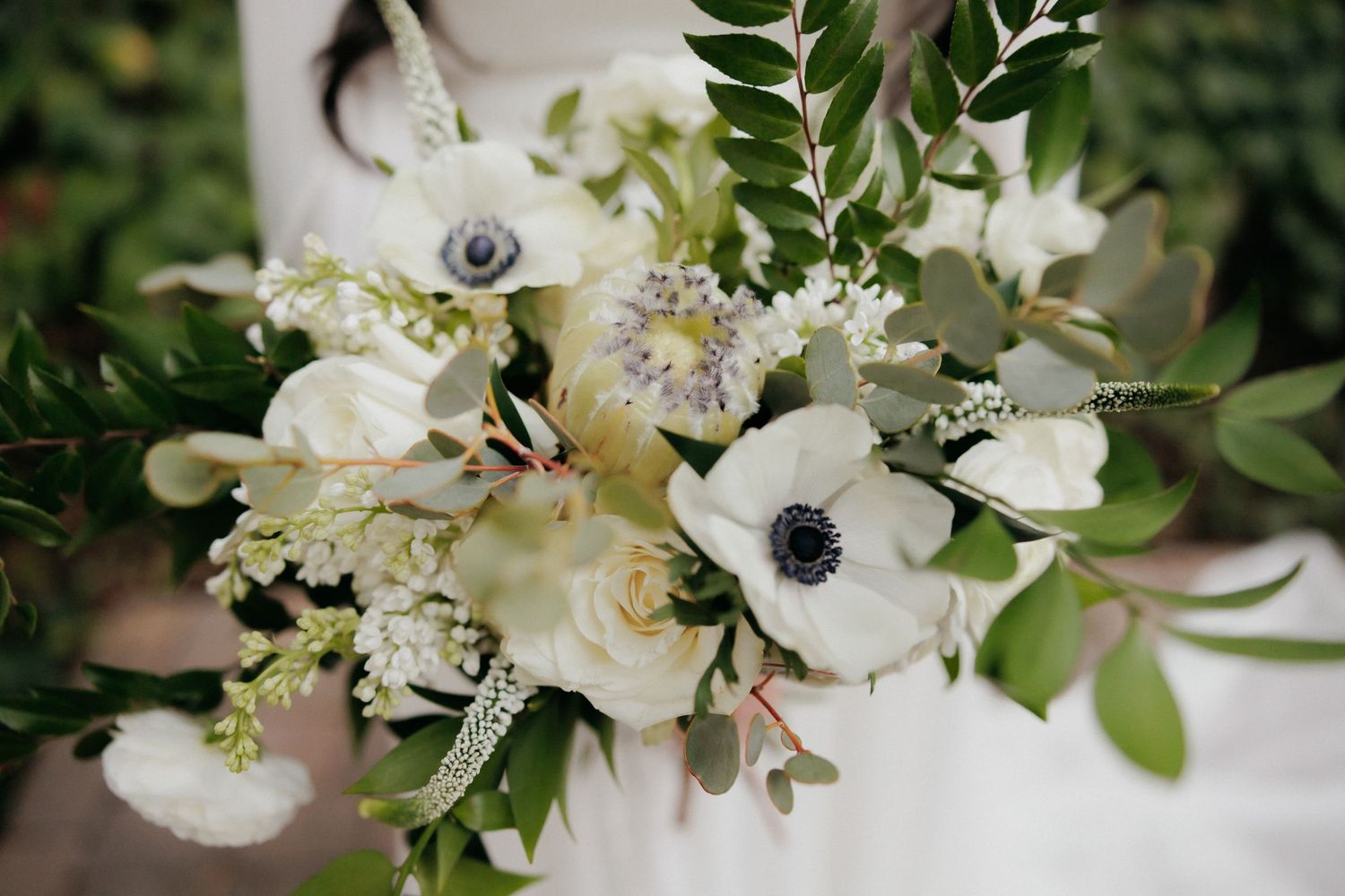 White anemone flower and greenery bouquet with buds arranged on a light neutral surface.